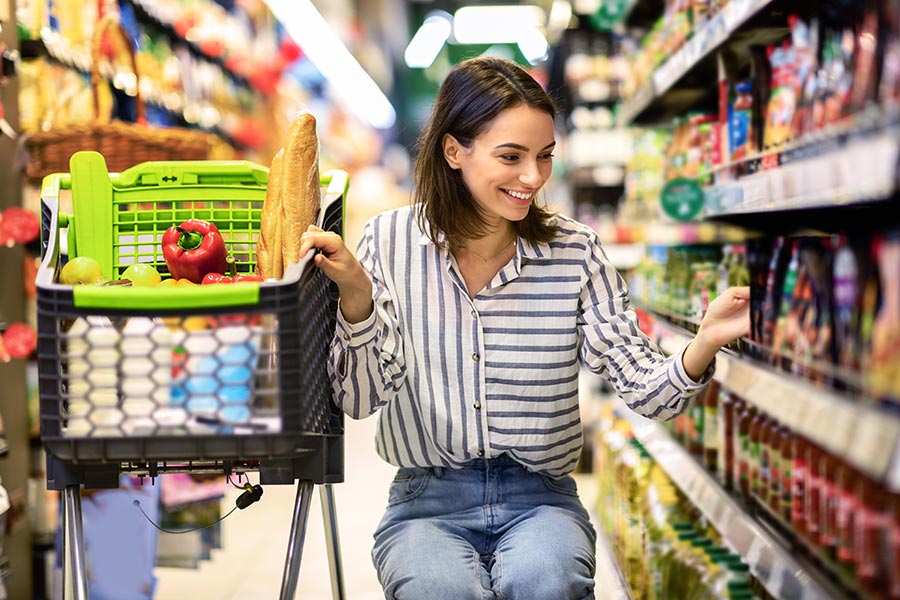 Frau kniet lächelnd vor einem Regal im Supermarkt