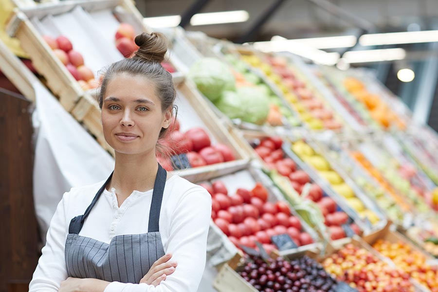Mitarbeiterin im Supermarkt posiert vor der Obst- und Gemüseabteilung